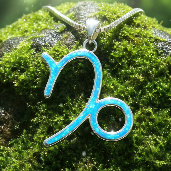 Close-up of the Capricorn glyph pendant inlaid with blue opal in a sterling silver setting, resting on moss