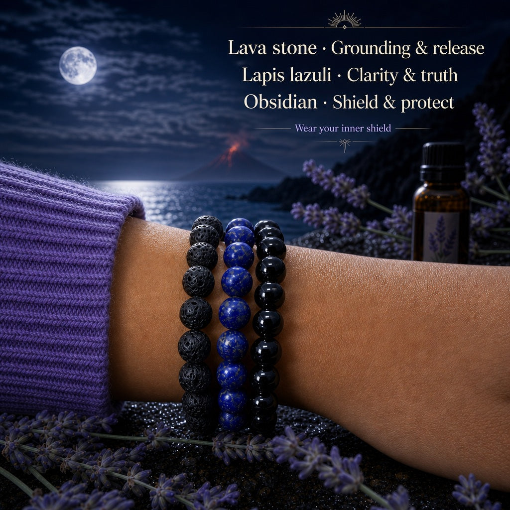 Lava stone, lapis lazuli and obsidian bead bracelets stacked on a wrist beside lavender and a bottle of essential oil