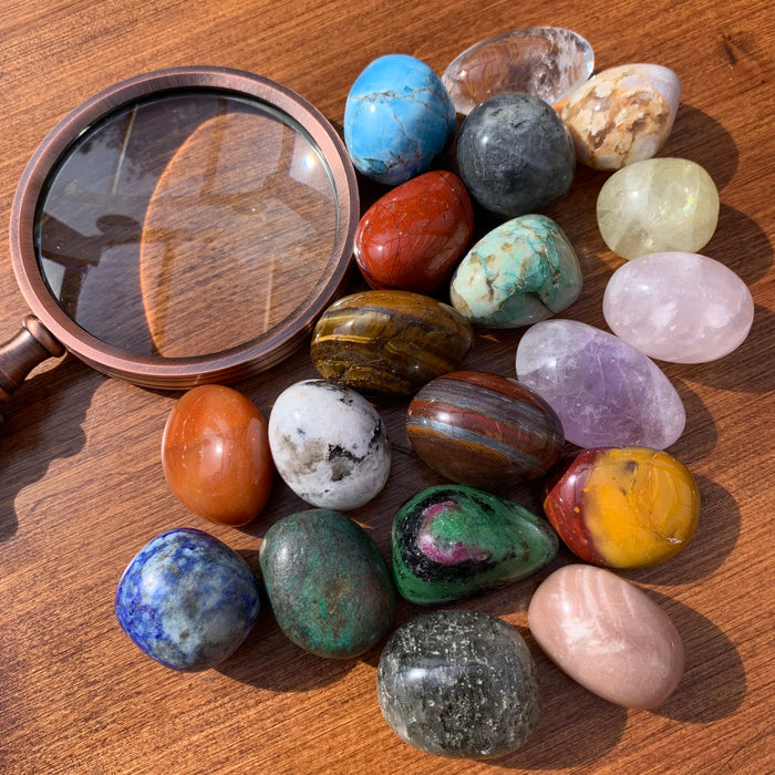 The nineteen tumbled stones gathered beside a brass magnifying glass on a wooden table