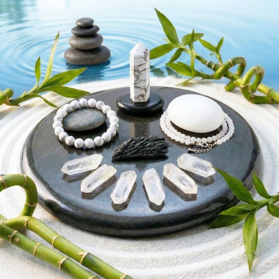 The full set on a black stone tray: a howlite point, howlite bead bracelet, white palmstone, white jade bead necklace, black kyanite fan and six clear quartz crystals, with bamboo and raked sand