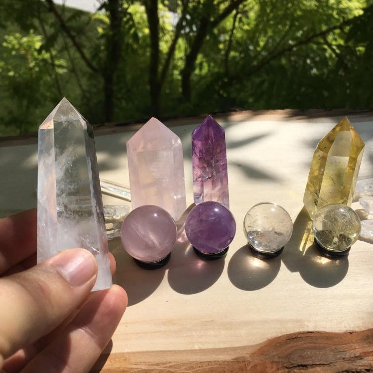 A clear quartz point held up in one hand beside the rose quartz, amethyst and citrine points and the four mini spheres