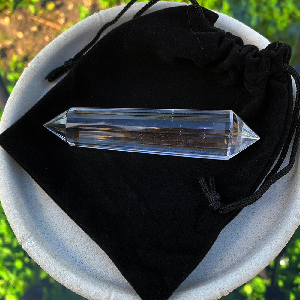 A longer Vogel quartz wand resting on its black velvet drawstring pouch in a white stone dish