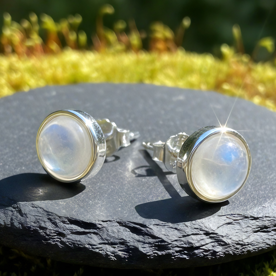 Macro view of both moonstone studs on dark slate, showing the domed stones, smooth silver bezels and the posts with their backings