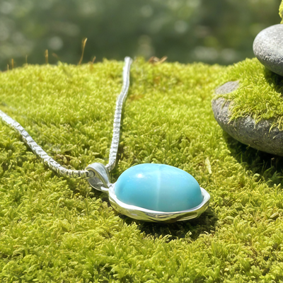 Side view of the domed larimar cabochon in its sterling silver bezel, resting on moss