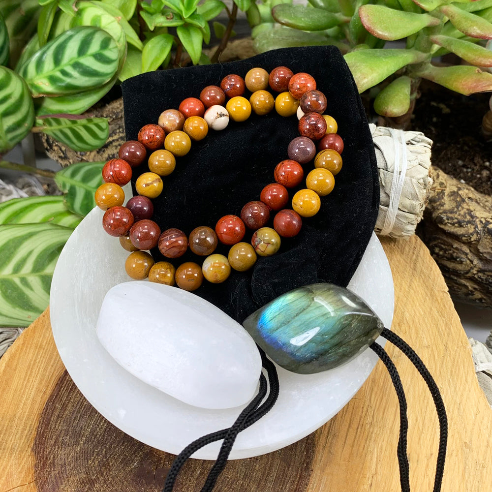 Golden mookaite and red earth mookaite mala bracelets on a black velvet pouch with a white selenite ellipse and a blue-flashing labradorite cabochon