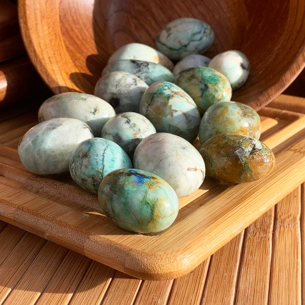 A pile of phoenix jasper ellipses spilling from a wooden bowl onto a bamboo tray, ranging from pale cream to teal green and golden brown