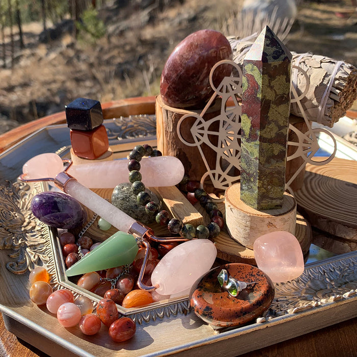 A past box with a red jasper egg, a bloodstone tower, a wooden sacred geometry grid, bracelets, a pendulum and tumbled stones