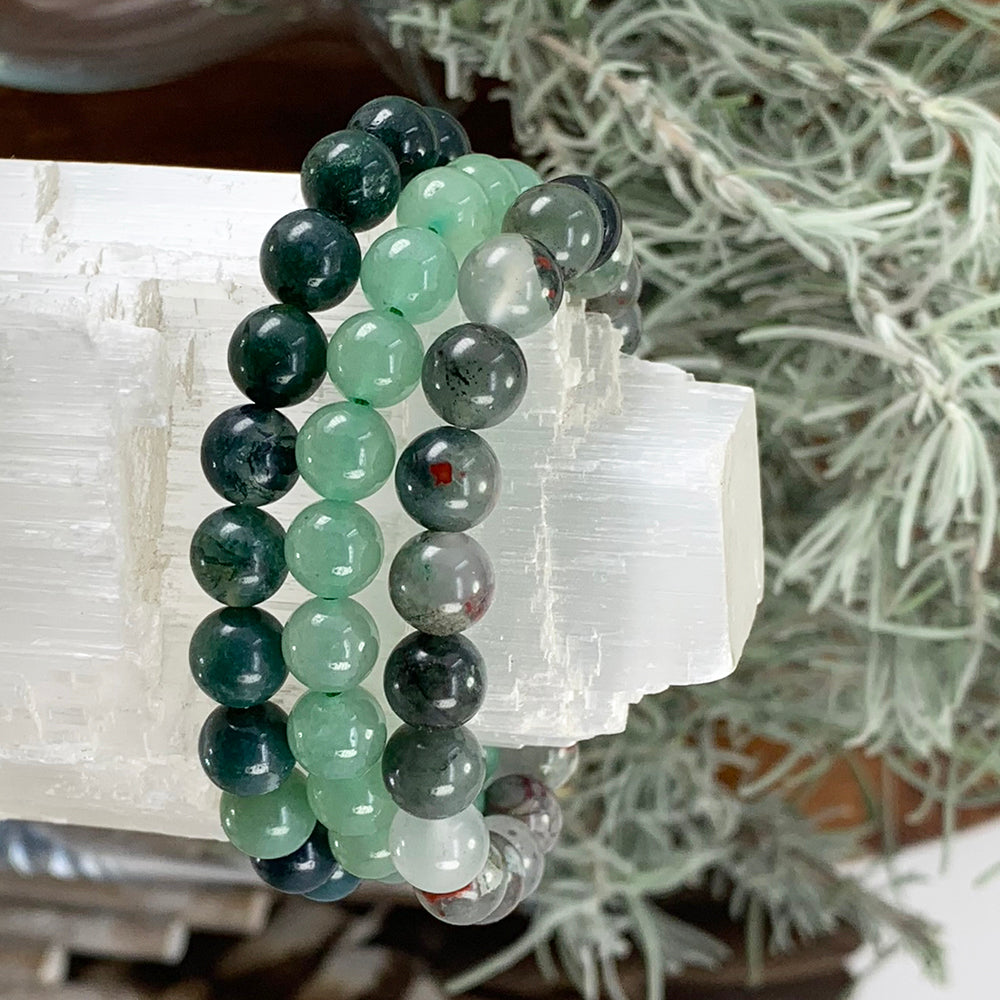 Moss agate, green aventurine and African bloodstone bead bracelets stacked on a selenite bar