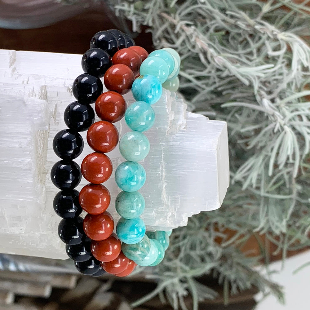 Black obsidian, red jasper and amazonite bead bracelets stacked on a selenite log