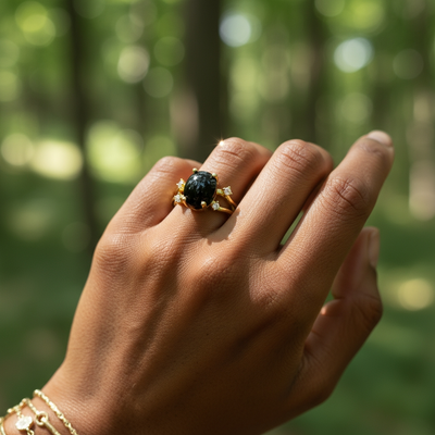 The black onyx and gold ring worn on a hand in a sunlit forest, with gold bracelets at the wrist