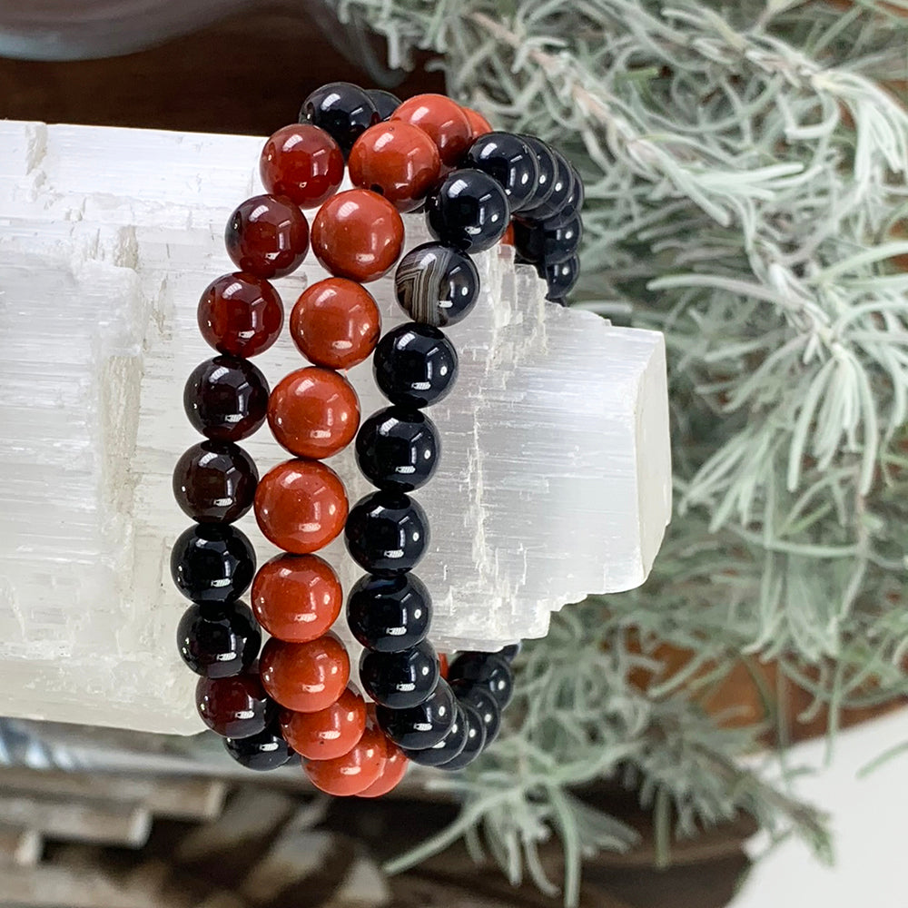 Black agate, red jasper and black stripe agate bead bracelets stacked on a selenite bar