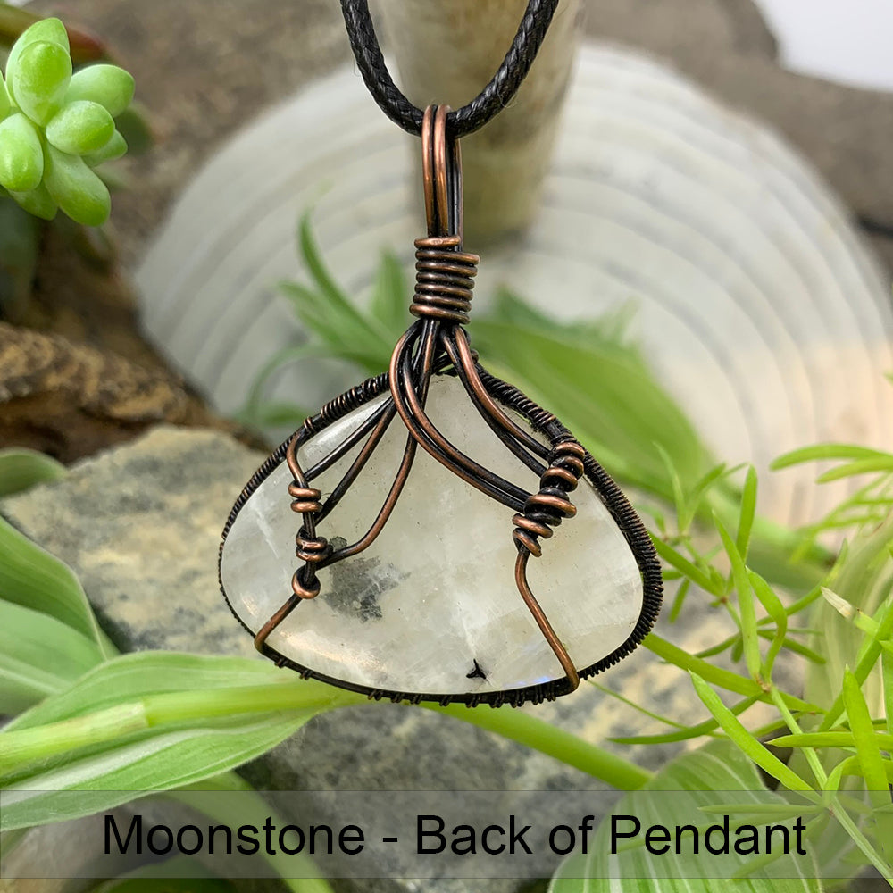 The back of the moonstone pendant, showing copper wires coiled and curving across the stone to hold it in its frame