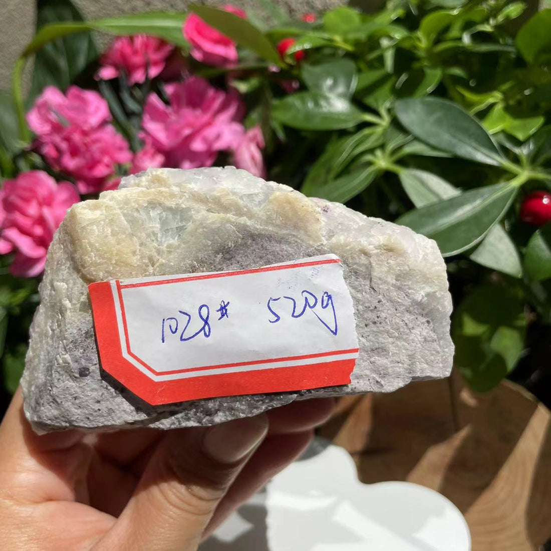 The underside of the fluorite cluster held in a hand, with its handwritten tag reading 1028 and 520 g