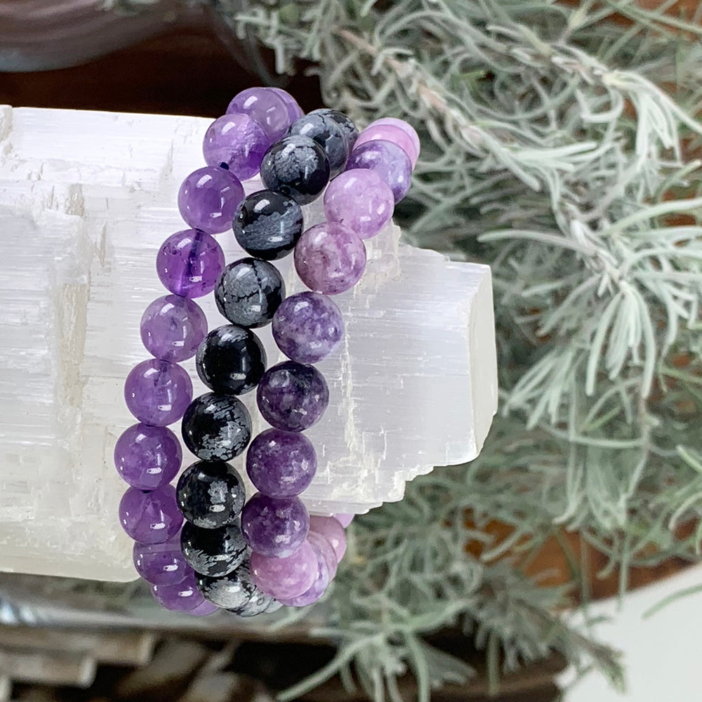 Amethyst, snowflake obsidian and lepidolite bead bracelets stacked on a selenite log
