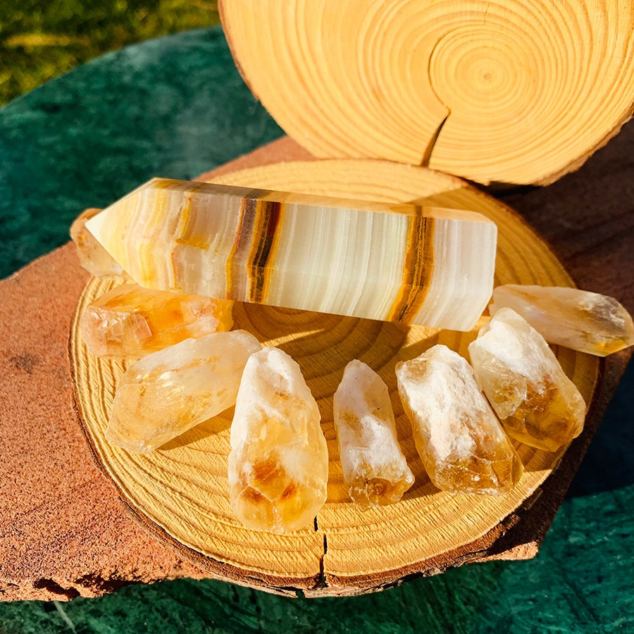 A banded cream and honey Afghanistan jade point lying on a wood slice with eight raw golden citrine shards around it