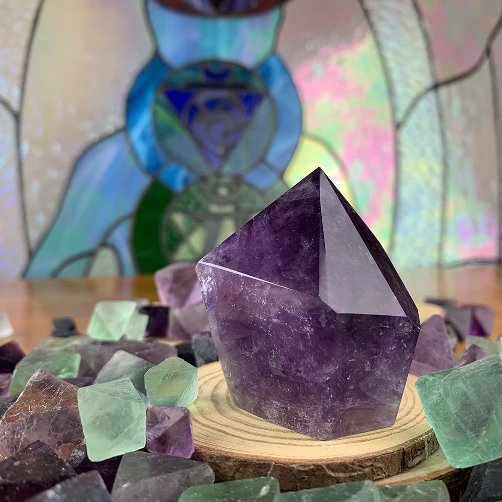 Deep purple amethyst freeform point with a polished faceted tip, standing on a wood slice
