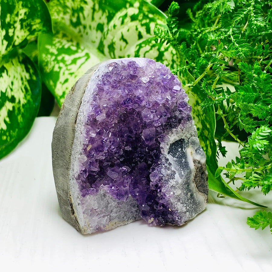 An amethyst geode freeform standing upright, its purple crystal face framed by smooth grey stone
