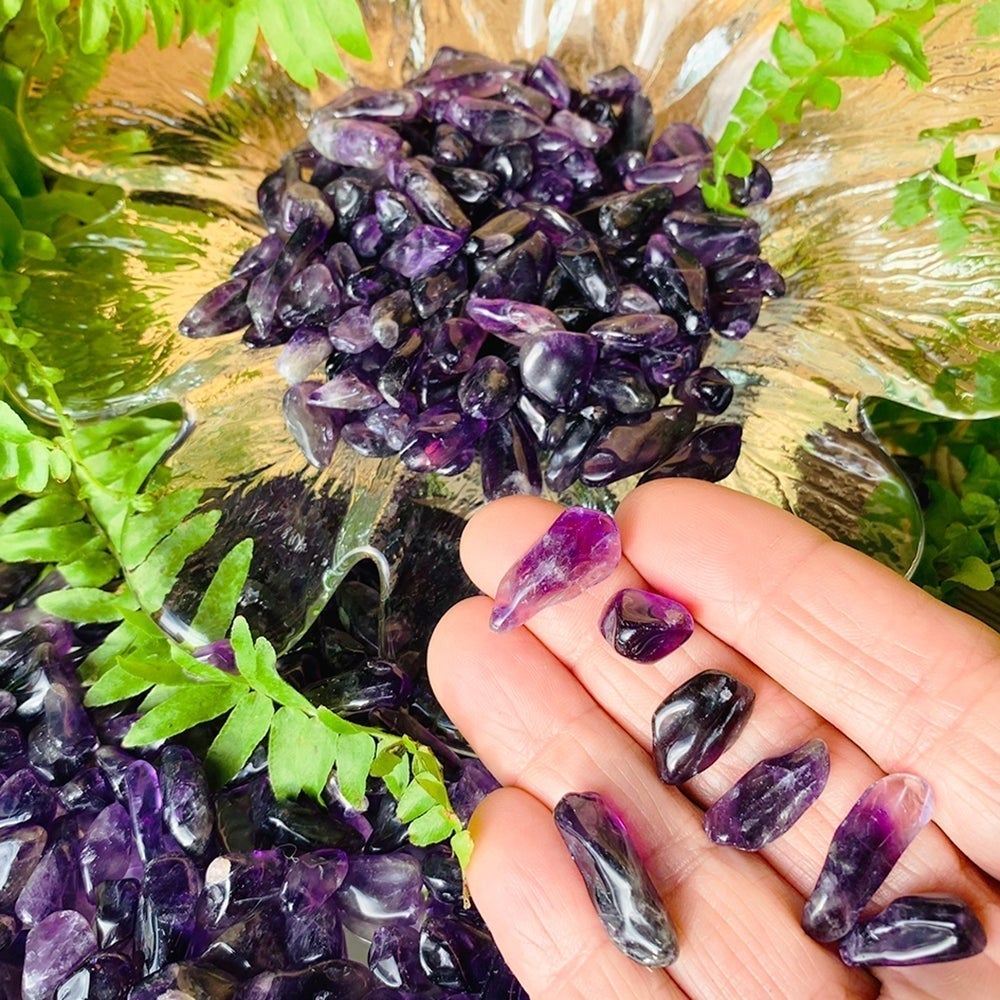 Small polished amethyst mini gemstones resting on fingertips beside a glass dish piled with more