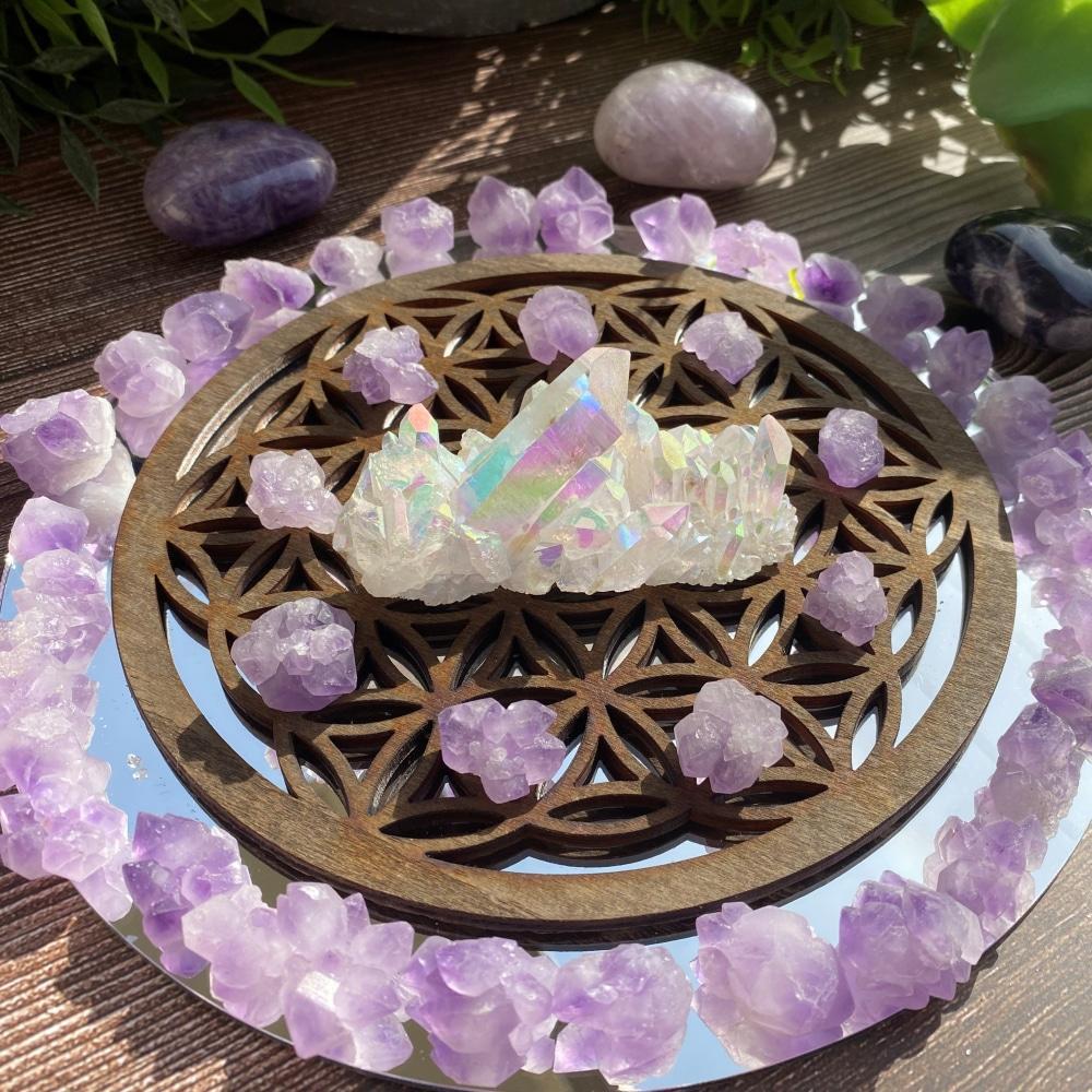 An angel aura quartz cluster at the center of a crystal grid, surrounded by a ring of pale lavender amethyst fairy clusters