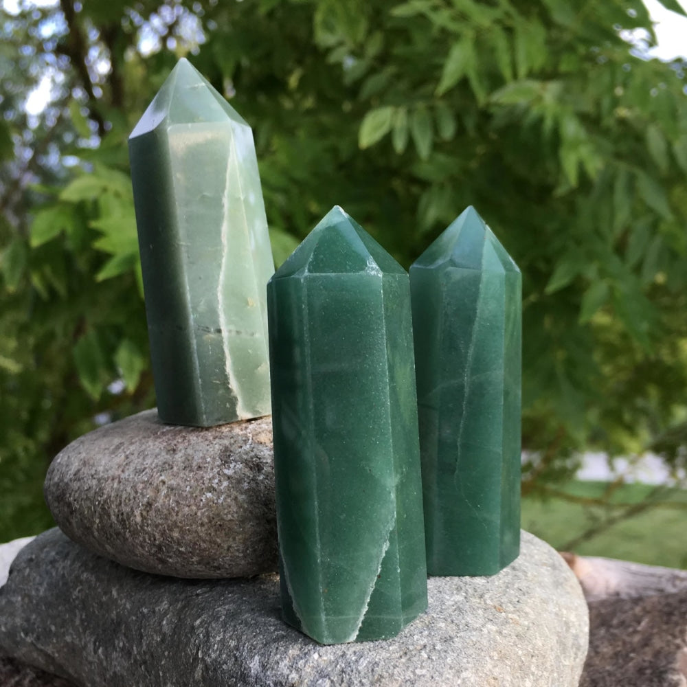 Three green aventurine points in lighter and deeper greens standing together on a stone outdoors