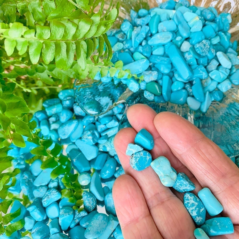 A few blue howlite mini gemstones resting on the fingers of an open hand above a bowl of more stones