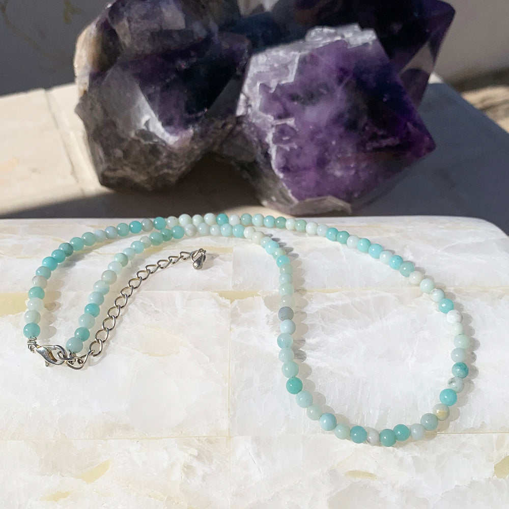 A Caribbean jasper bead necklace in soft aqua, teal and cream, laid out with its silver clasp and extender chain on white stone