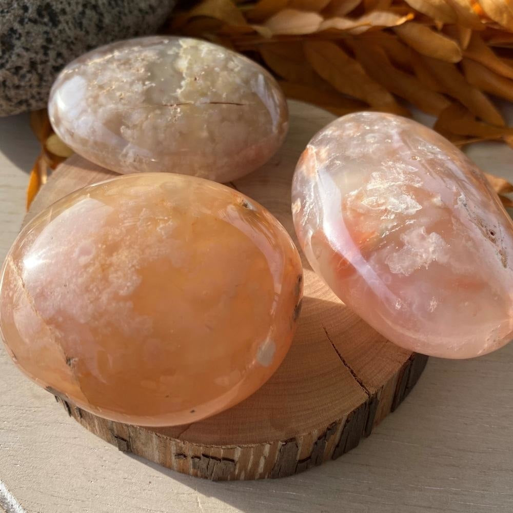 Three cherry blossom agate palmstones on a wood slice, each with its own mix of peach, pink and cream blossoms
