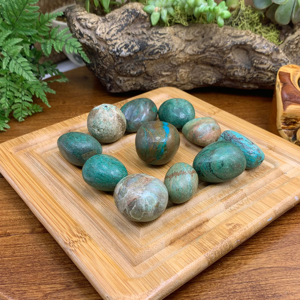 A dozen chrysocolla tumbled stones on a bamboo tray, each a different mix of blue, green and earthy brown
