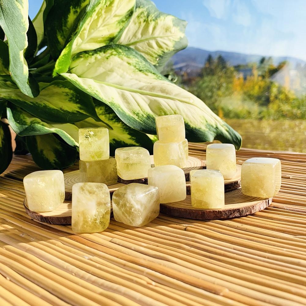 Translucent pale golden citrine tumbled cubes stacked on wood slices in sunlight beside a leafy plant