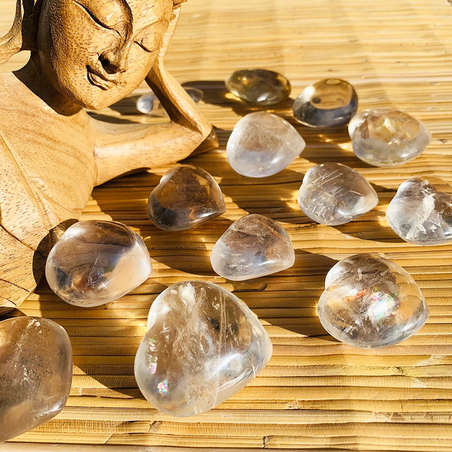 A dozen clear quartz hearts scattered on a bamboo mat beside a carved wooden Buddha, each with its own veils and clarity