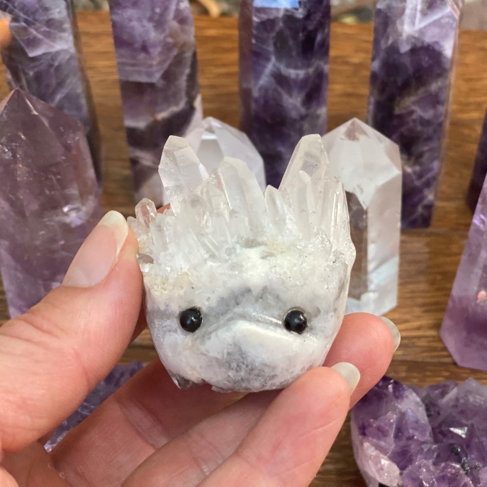 A clear quartz hedgehog with crystal-point quills and black bead eyes held between finger and thumb