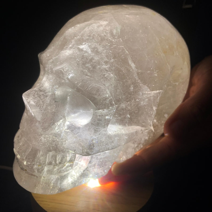 A hand resting against the side of the lit quartz skull, showing its size