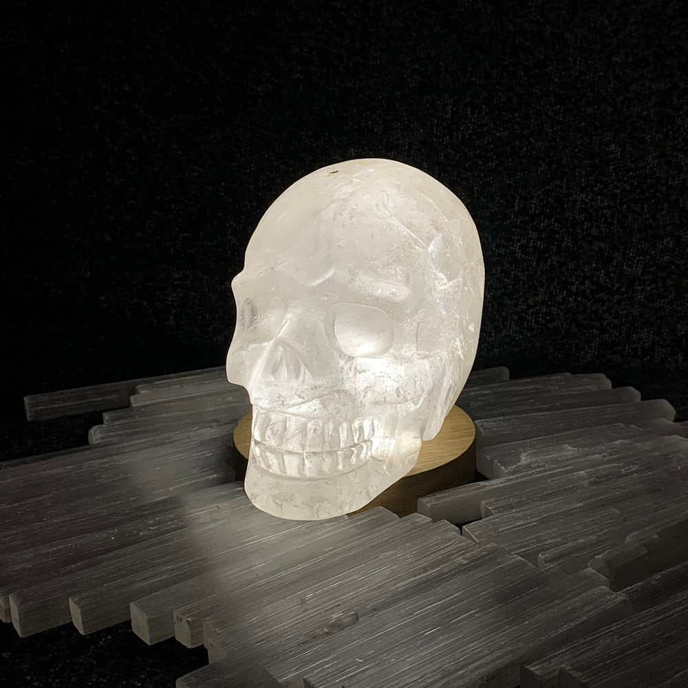 The quartz skull glowing on a light base, surrounded by selenite slabs in a dark room