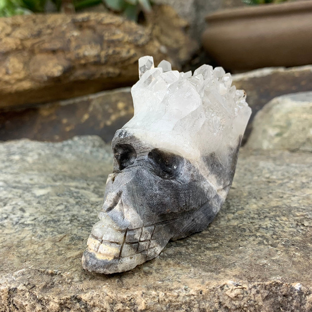 A grey and white hand-carved crystal skull with a crown of clear crystal shards, resting on a stone ledge