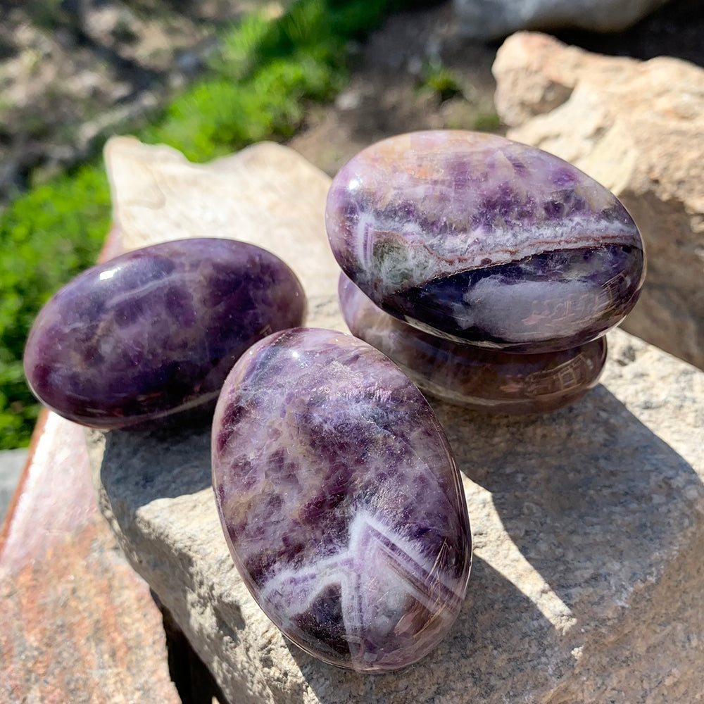 Three dream amethyst palmstones on a sunlit rock, each with its own sweep of purple and white bands