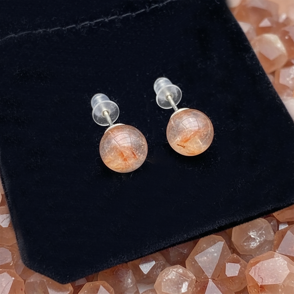 The two fire quartz studs on their posts with clear earring backs, laid on a black velvet drawstring pouch