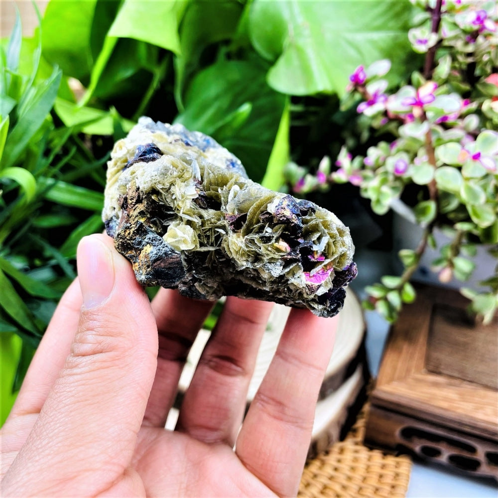 Side view of the fosfosiderite specimen held in a hand, showing layered green crystal blades with darker iridescent patches