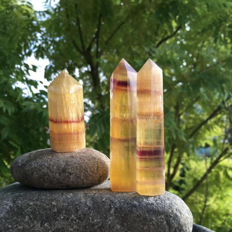 Three golden fluorite points on river stones, each banded differently in honey gold, cream and violet