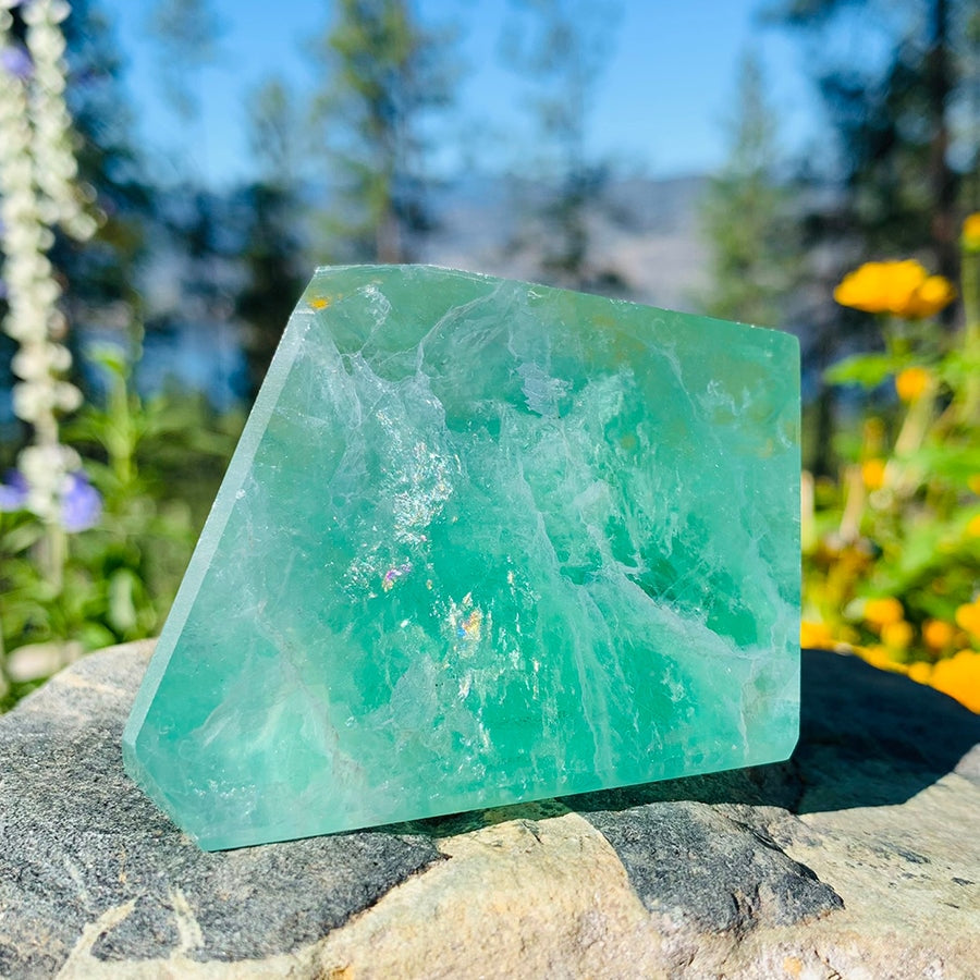 A freeform green fluorite chunk in sunlight on a rock, its translucent green bands and veils glowing