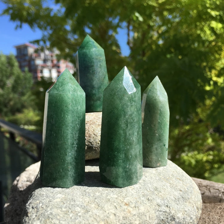 Four green strawberry quartz points of different heights and shades standing on river stones