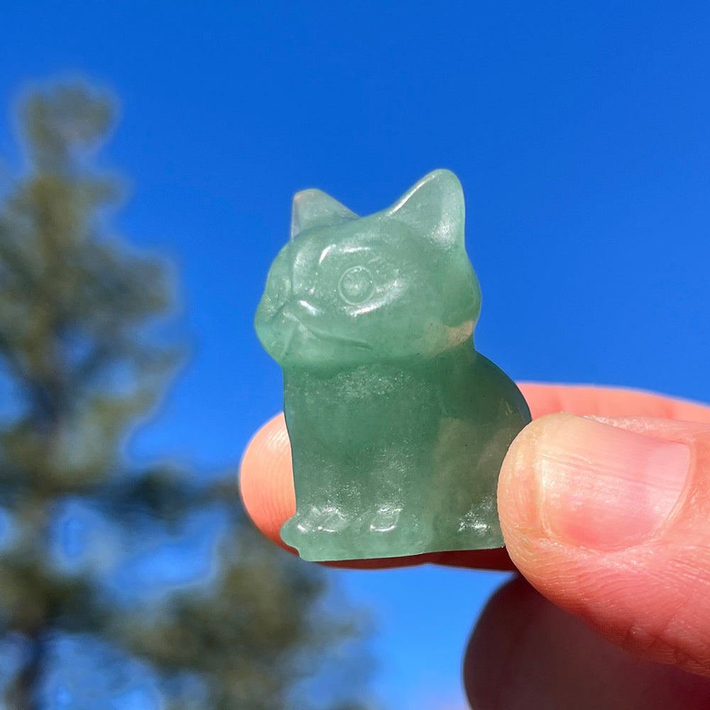 The green quartz cat held between finger and thumb against a blue sky