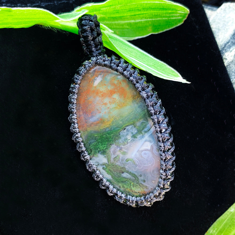 Close-up of a macramé-wrapped moss agate pendant showing green moss-like inclusions and warm orange tones