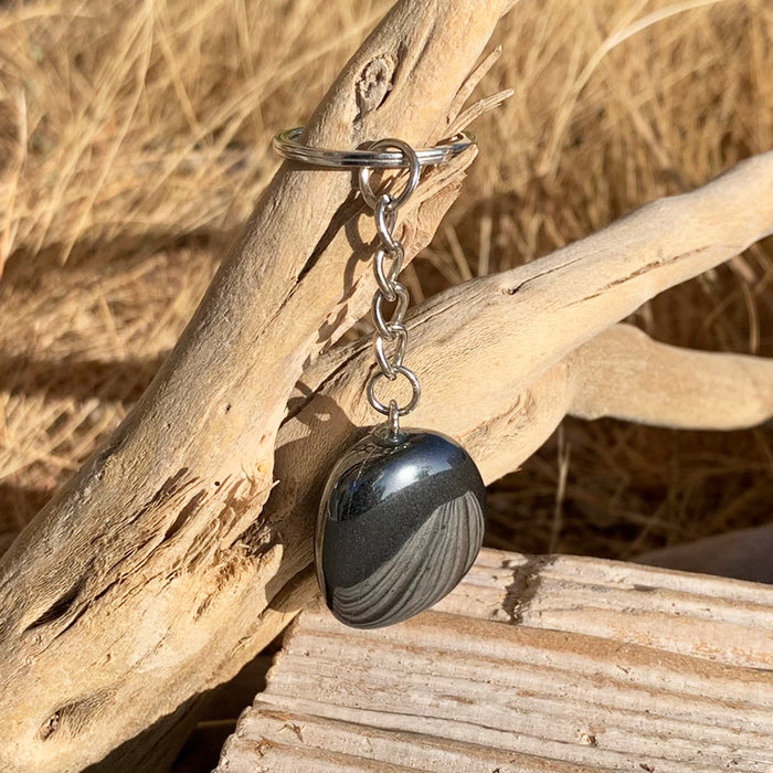 A polished silver-grey hematite stone on a keychain hanging from driftwood