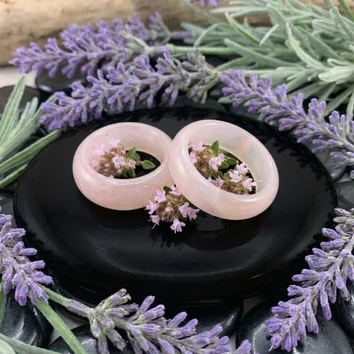 Two pale pink agate rings on a dark dish surrounded by lavender