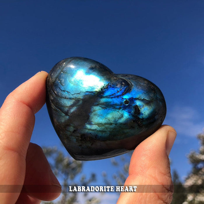 A labradorite heart held between finger and thumb against a blue sky