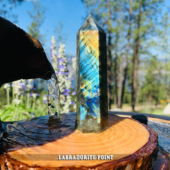 A labradorite point standing on a wooden slice beside a small water fountain outdoors