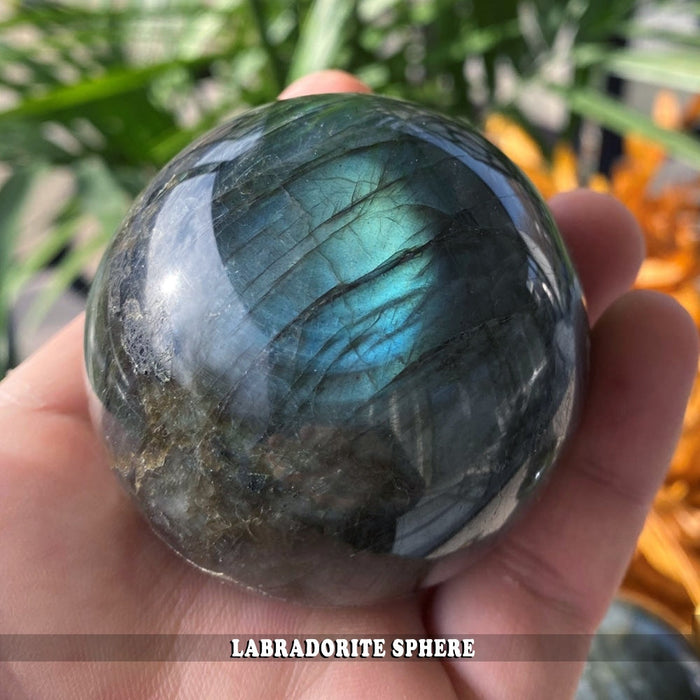 A polished labradorite sphere resting in an open palm, glowing teal