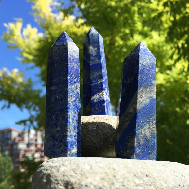 Three polished lapis lazuli points standing on a stone in the sun, deep blue with white and gold flecks