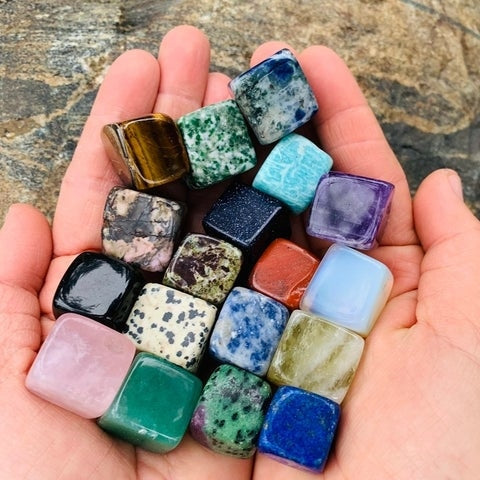An open hand holding nineteen colourful tumbled crystal cubes, including a lapis lazuli cube