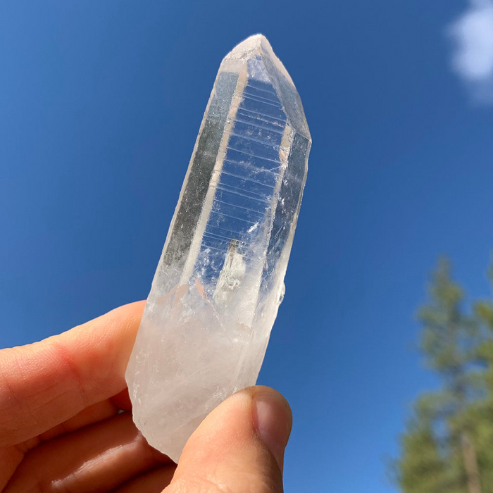 A clear Lemurian seed quartz point held up against a blue sky